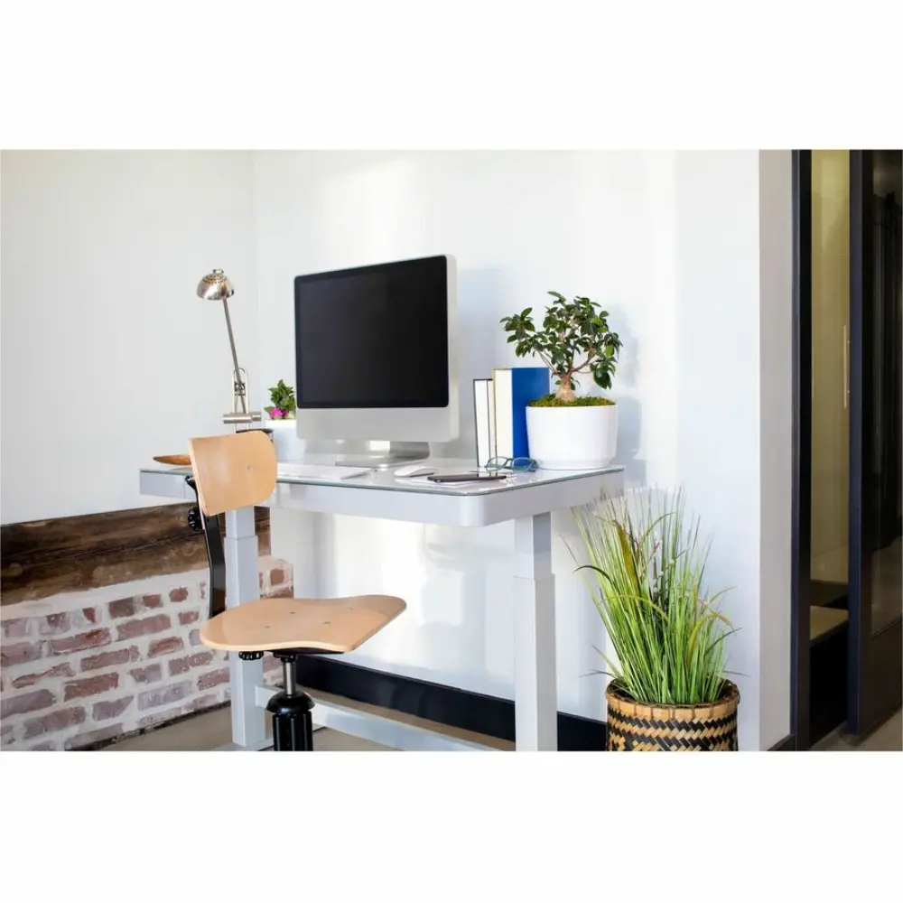 Overhead view of a clean white desk on a gray floor with keyboard, monitor, and office supplies.