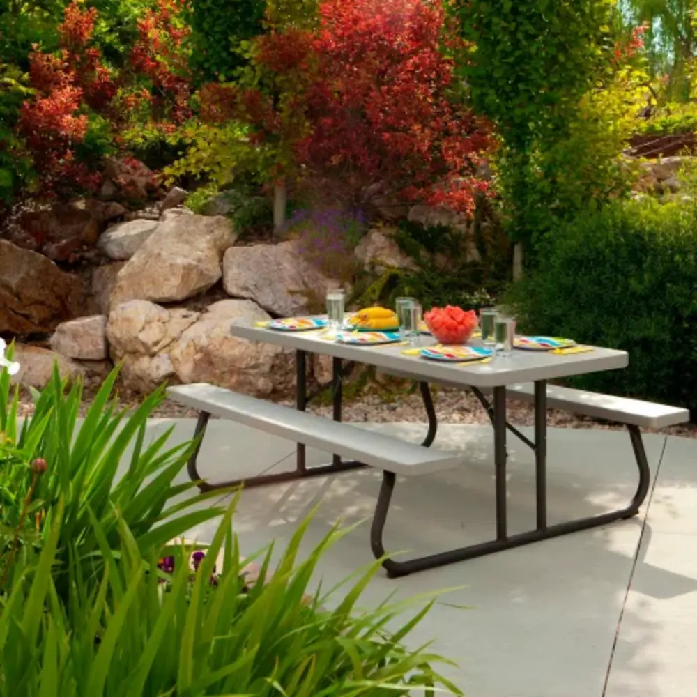Outdoor dining setup on a grey picnic table with matching benches in a garden setting, with plates and glasses